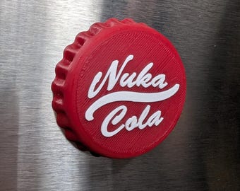May include: A red bottle cap with the words "Nuka Cola" in white script. The cap has a textured surface and a ridged edge. The image is a close-up shot of the bottle cap.