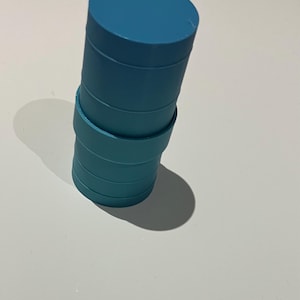 May include: A stack of teal-colored, cylindrical objects. The objects are stacked on top of each other, with a slightly angled perspective. The top cylinder is a solid teal, while the lower cylinders have a slightly lighter shade of teal.