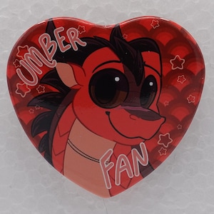 Puede incluir: Un pin en forma de coraz&oacute;n con un personaje de drag&oacute;n rojo y negro de dibujos animados con ojos grandes. El fondo es rojo oscuro con un patr&oacute;n de ondas y estrellas peque&ntilde;as. El texto "UMBER" est&aacute; impreso arriba y "FAN" abajo en blanco.