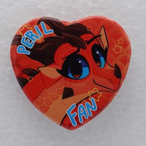 Puede incluir: Un pin en forma de coraz&oacute;n que presenta un personaje de drag&oacute;n estilizado de color naranja y rojo con grandes ojos azules. El texto PERIL est&aacute; impreso en azul claro en la parte superior izquierda y la palabra FAN en azul claro abajo a la derecha.