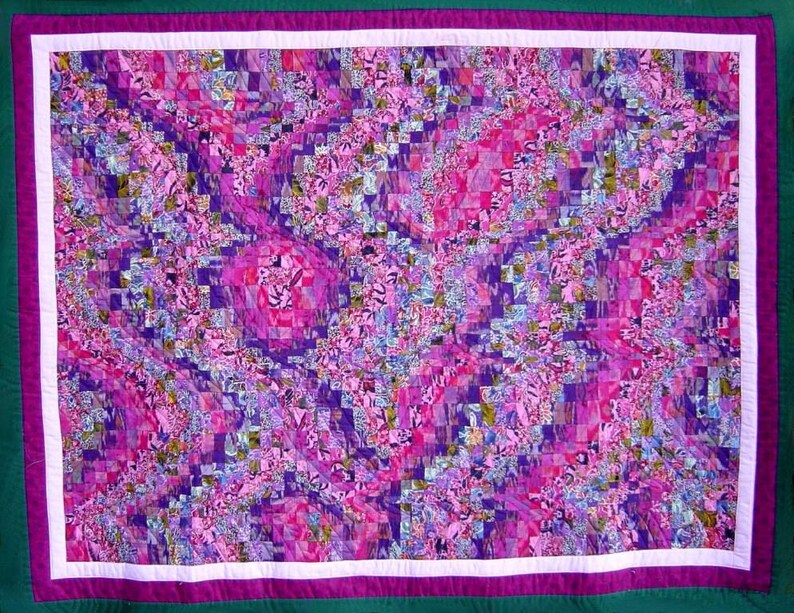 May include: A handmade quilt with a vibrant, abstract design. The quilt features a patchwork of small squares in shades of pink, purple, and blue, creating a swirling pattern. It has a white border, a purple border, and a green backing.