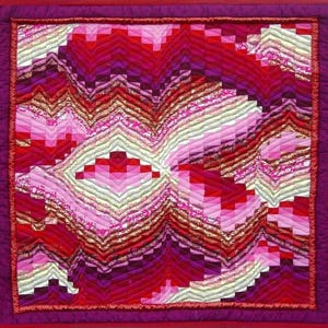 May include: A colourful handmade quilt with an abstract design. The quilt showcases a patchwork of red, pink, and purple fabrics arranged in a geometric pattern. The edges are finished with a deep red border, creating a striking visual contrast.