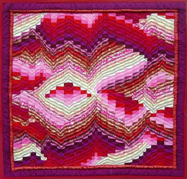May include: A colourful handmade quilt with an abstract design. The quilt showcases a patchwork of red, pink, and purple fabrics arranged in a geometric pattern. The edges are finished with a deep red border, creating a striking visual contrast.
