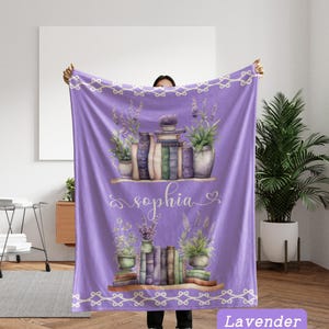 May include: A lavender-colored blanket featuring a watercolor design of books, plants, and the name "Sophia." The design includes two shelves with stacks of books and potted plants, with a decorative border along the top and bottom.