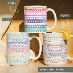 May include: Three white ceramic mugs featuring colorful horizontal patterns. The top mug displays the text 'TODAY' in repeating rows. The bottom two mugs feature various geometric line designs in blue, green, red, and purple. A lemon slice rests on the right mug.