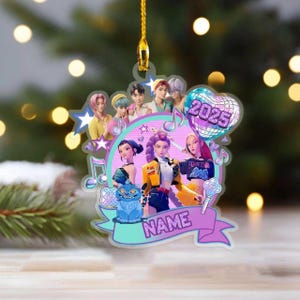 May include: A personalized Christmas ornament featuring a group of animated figures, musical notes, and the year 2025. The ornament has a ribbon with the word "NAME" and a blue cat. The ornament is hanging from a gold string.