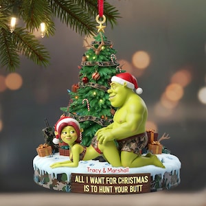 Pode incluir: Enfeite de Natal com Shrek e Fiona com gorros de Papai Noel, com uma árvore de Natal decorada. O enfeite tem o texto "ALL I WANT FOR CHRISTMAS IS TO HUNT YOUR BUTT".