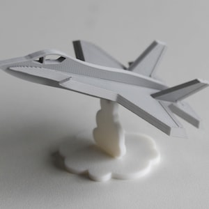 Op de afbeelding: Een wit plastic model van een straaljager op een witte plastic basis. Het model is gedetailleerd en heeft een realistisch uiterlijk.