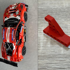 Könnte beinhalten: Ein rotes Spielzeug-Rennauto mit weißen und blauen Akzenten, schwarzen Rädern und Sponsorenlogos. Daneben ein rotes Kunststoffwerkzeug mit einem weißen Klebestreifen.