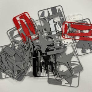May include: A collection of plastic model aeroplane kits on sprues, featuring various aircraft parts in grey, red, white, and black. The frames contain moulded components for assembly, including wings, fuselages, and tail sections for multiple models.