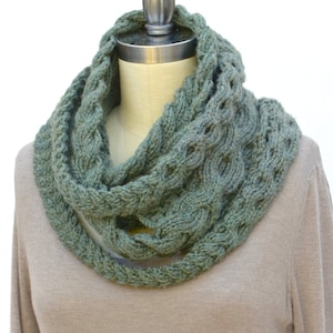 May include: A green knitted infinity scarf with a cable knit pattern. The scarf is displayed on a mannequin.