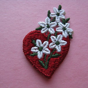 May include: Red felt heart with embroidered white flowers and green stems.