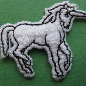 May include: White embroidered unicorn patch with black outline. The unicorn is standing with its head turned to the side and its horn pointing forward.