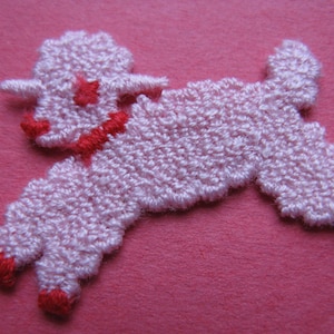May include: A pink felt lamb applique with red embroidered details. The lamb is standing on its hind legs with its front legs raised.