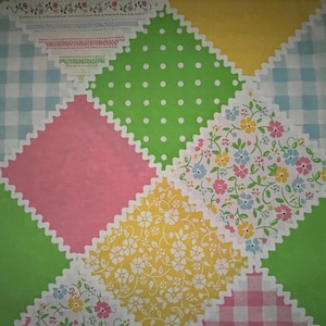 May include: A patchwork fabric with a variety of patterns and colors. The design includes squares of pink, green, yellow, and blue gingham, along with floral and polka dot patterns. The edges of the squares are scalloped.