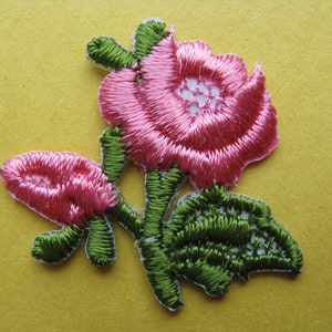 May include: Pink embroidered rose flower applique with green leaves and stems.
