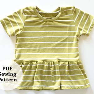 May include: A light green and white striped t-shirt with short sleeves and a ruffled hem. The text "PDF Sewing Pattern" is displayed on the lower left side of the shirt. The shirt is made of a soft, lightweight fabric.