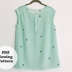 May include: A mint green sleeveless blouse with a button-up front and a scattered pattern of black and gray triangles. The blouse is hanging on a wooden hanger.