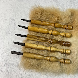 Peut inclure: Ensemble de six outils de sculpture à manche en bois avec des lames en métal noir. Les outils sont disposés sur une surface en fourrure brune.