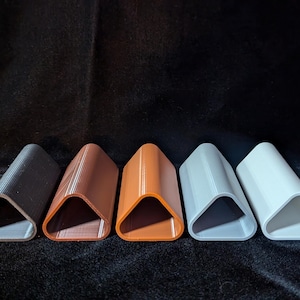 May include: Five triangular-shaped, 3D printed, decorative objects in different colors. The objects are arranged in a row from left to right: black, brown, orange, white, and light gray.
