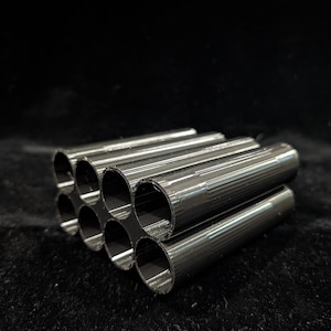 May include: A cluster of nine metallic, cylindrical tubes arranged in a grid pattern. The tubes are a dark, reflective color, possibly steel or a similar metal. The ends of the tubes are visible, revealing their hollow interiors. The background is a dark, solid color.
