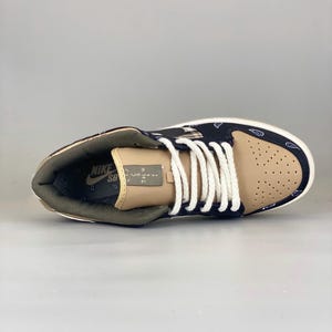 K&ouml;nnte beinhalten: Ein Paar Nike SB Dunk Low Sneaker. Der Schuh hat eine Zehenbox aus beigem Wildleder, ein schwarz-wei&szlig;es Paisley-Muster auf den Seitenteilen und eine braune Wildlederferse. Das Nike SB-Logo ist auf der Zunge sichtbar.