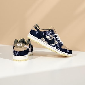 K&ouml;nnte beinhalten: Ein Paar Nike Dunk Low Sneaker. Die Schuhe haben eine marineblaue und beige Farbgebung mit einem Paisley- und Karomuster. Der Nike Swoosh ist schwarz. Die Sohlen sind cremefarben.