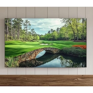 Könnte beinhalten: Ein Fernsehbildschirm zeigt ein Panoramabild eines Golfplatzes mit einer Steinbrücke über einem Teich. Der Platz ist grün und üppig, mit Bäumen, die die Ränder säumen. Der Himmel ist blau mit weißen Wolken.