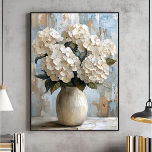 Pode incluir: Um vaso de cerâmica branco com um buquê de hortênsias brancas. O vaso tem uma superfície texturizada e está sentado em uma mesa com um fundo azul claro e branco.