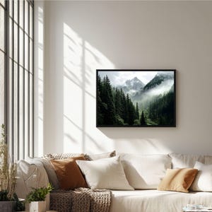 May include: A framed photograph of a mountain range with a misty forest in the foreground. The mountains are covered in snow and the forest is lush and green.
