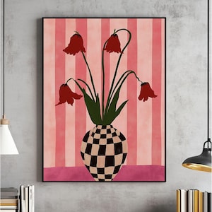 Può includere: Una stampa artistica incorniciata con un vaso con un motivo a scacchi in bianco e nero, che contiene fiori rossi con steli e foglie verdi. Lo sfondo presenta strisce rosa verticali. L'opera d'arte è esposta su un muro grigio.