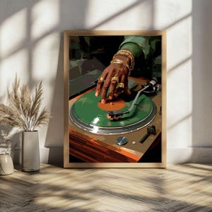 May include: A framed art print depicts a DJ's hand adorned with gold jewelry, poised over a green vinyl record on a turntable. The artwork features a warm color palette with shades of brown, green, and gold, creating a vintage aesthetic. The print is displayed on a wooden floor.