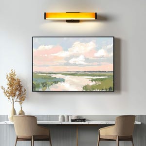 May include: A framed abstract landscape painting with a light blue, pink, and white sky with fluffy clouds. The painting depicts a green marsh with a winding river flowing through it.