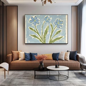 Puede incluir: Una pintura de tres flores azules con tallos y hojas verdes sobre un fondo azul claro. La pintura est&aacute; enmarcada y colgada en una pared sobre un sof&aacute; de cuero marr&oacute;n con almohadas.