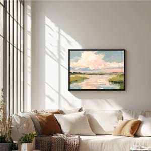May include: A framed painting depicting a landscape with a river, green grass, and a pink and blue sky with clouds. The painting is in a black frame and is hanging on a white wall.