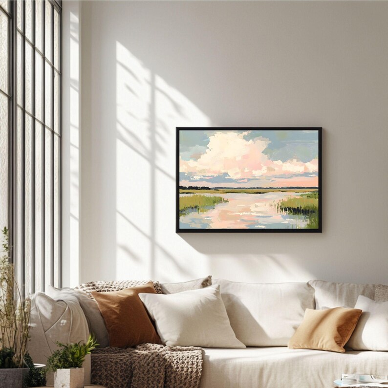 May include: A framed painting depicting a landscape with a river, green grass, and a pink and blue sky with clouds. The painting is in a black frame and is hanging on a white wall.
