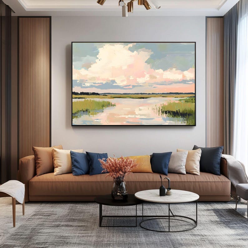 May include: A brown leather sofa with cushions in a variety of colours and textures, including blue, beige, and white. The sofa is positioned in front of a large painting depicting a landscape with a lake and a cloudy sky. The painting is framed in black.