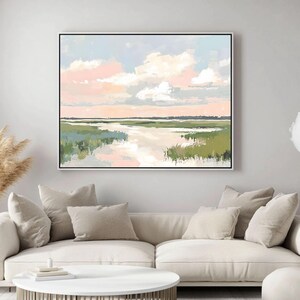 May include: Abstract landscape painting with a light blue sky, pink clouds, and a green marsh with a winding river. The painting is framed in a black frame.