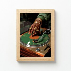 May include: A framed print featuring a DJ's hand adorned with gold rings and bracelets, manipulating a green vinyl record on a turntable. The artwork has a warm color palette with brown and green tones, and the frame is a light wood color.