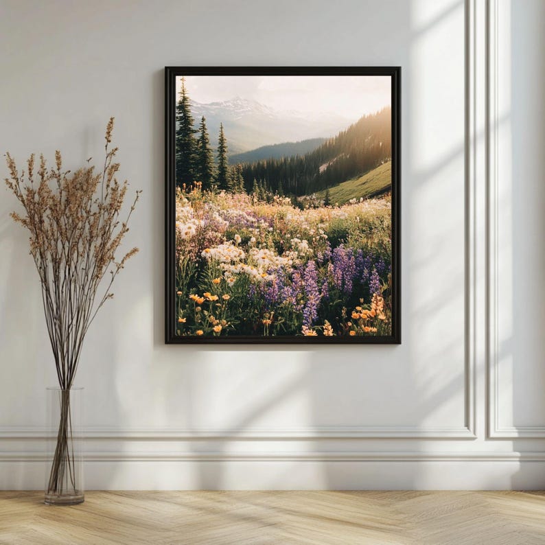 May include: A framed photograph of a mountain meadow with a variety of wildflowers in bloom. The meadow is in the foreground, with a mountain range in the background. The sky is a light blue with some clouds. The sun is shining brightly, and the flowers are in full bloom.