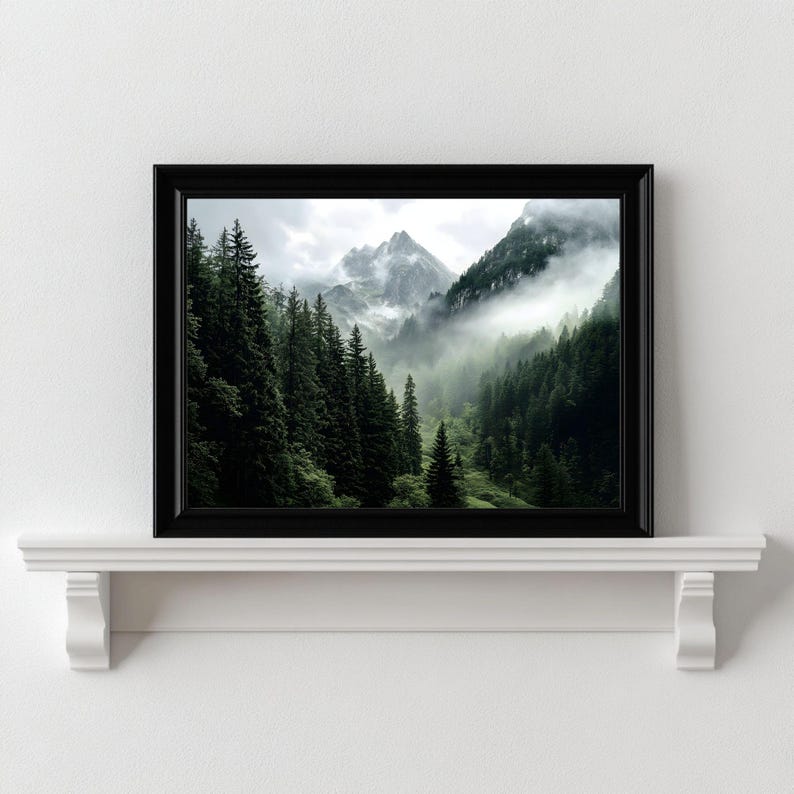 May include: A framed photograph of a misty mountain landscape with lush green trees in the foreground. The mountains are covered in clouds and fog, creating a sense of mystery and tranquility.