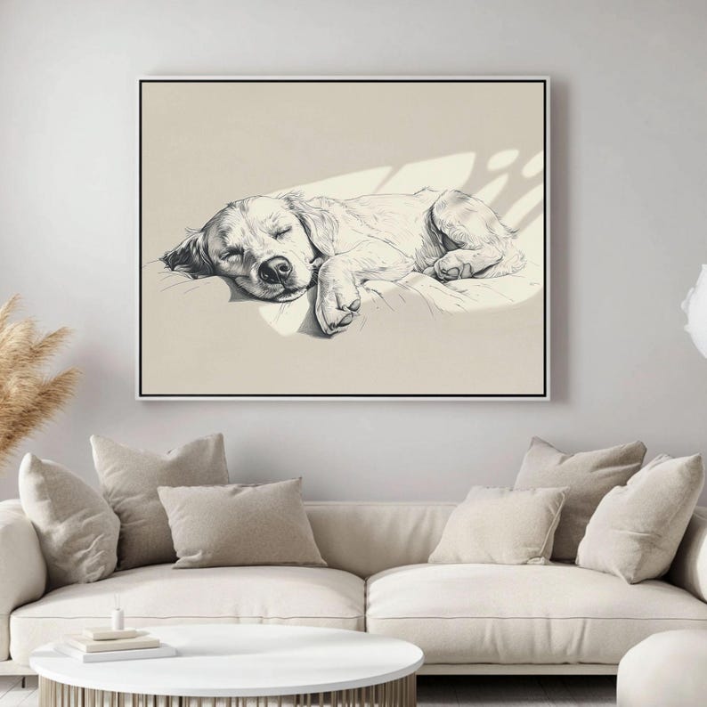 May include: A framed monochrome sketch of a sleeping dog. The dog is depicted lying down, eyes closed, on a light-coloured surface. The artwork is mounted on a wall above a white sofa with beige cushions.