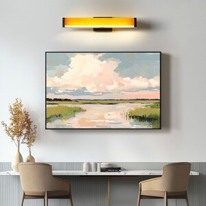 May include: A framed landscape painting depicting a river flowing through a grassy marsh with a large, fluffy pink and white cloud in the sky.