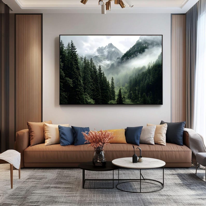 May include: A brown leather sofa with multiple pillows in various colors, including beige, blue, and cream. The sofa is positioned in front of a wall with a large framed print of a misty mountain landscape.