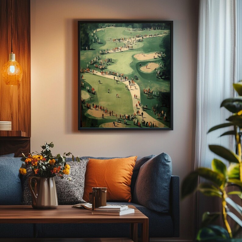 Może przedstawiać: Oprawiony wydruk przedstawiający pole golfowe. Grafika przedstawia zielone pole golfowe z licznymi ludźmi, drzewami i piaskownicami. Wydruk jest w czarnej ramie i wisi nad niebieską sofą z pomarańczowymi i szarymi poduszkami.