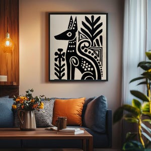 May include: Black and white abstract art print of a dog-like figure with decorative floral elements. The artwork is framed in a black square frame and hangs on a neutral wall. The image is part of a home decor collection.