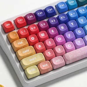 May include: A white mechanical keyboard with colorful keycaps. The keycaps are arranged in a rainbow gradient, with each row transitioning through different colors. Individual keycaps are scattered around the keyboard.