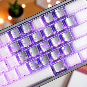 May include: A close-up of a mechanical keyboard with silver keycaps featuring purple butterfly designs. The keyboard has white keys and a purple backlight. The keyboard is a modern design.