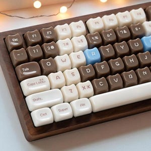 May include: A close-up of a mechanical keyboard with a wooden frame. The keycaps are a mix of brown, white, and light blue. The keyboard has a retro aesthetic, with a focus on the keycaps' unique color scheme and design. The keys are labeled with letters, numbers, and symbols.