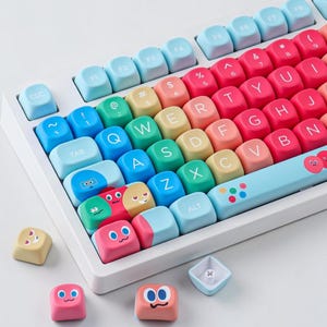 May include: A white mechanical keyboard with colorful keycaps. The keycaps are a gradient of colors, including blue, yellow, and red. Some keycaps feature cartoon faces. The keyboard has a standard QWERTY layout.